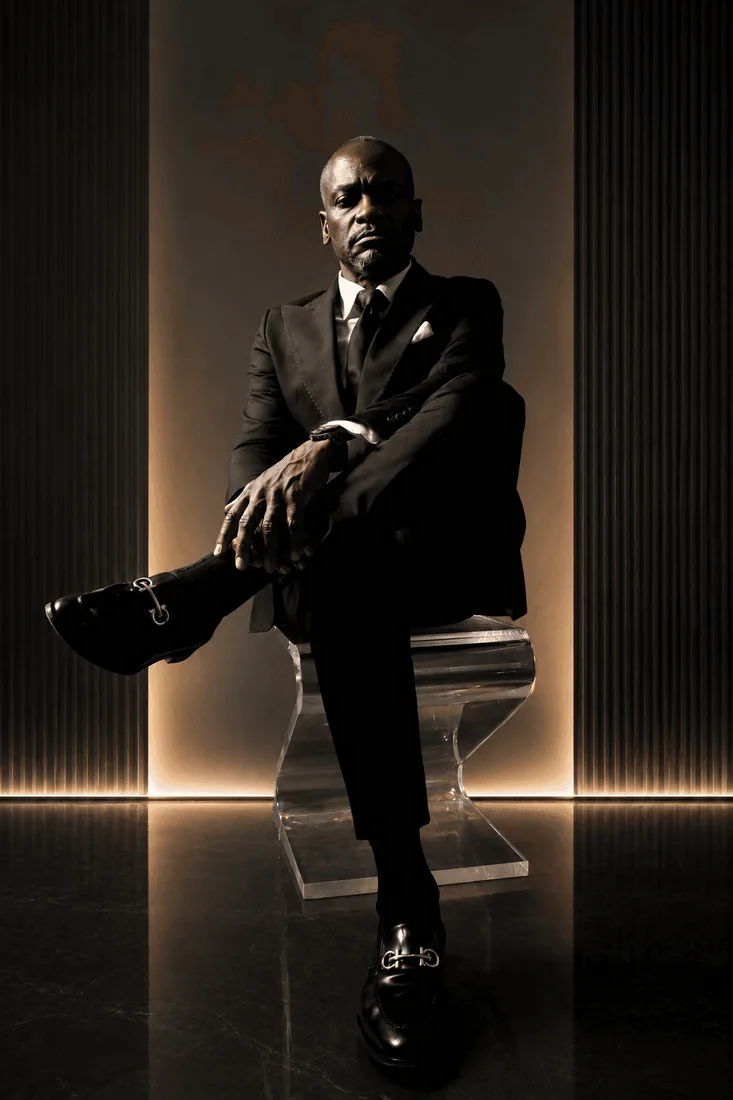 Dr. Glenn Toby seated in a black suit against a warm backlit wall